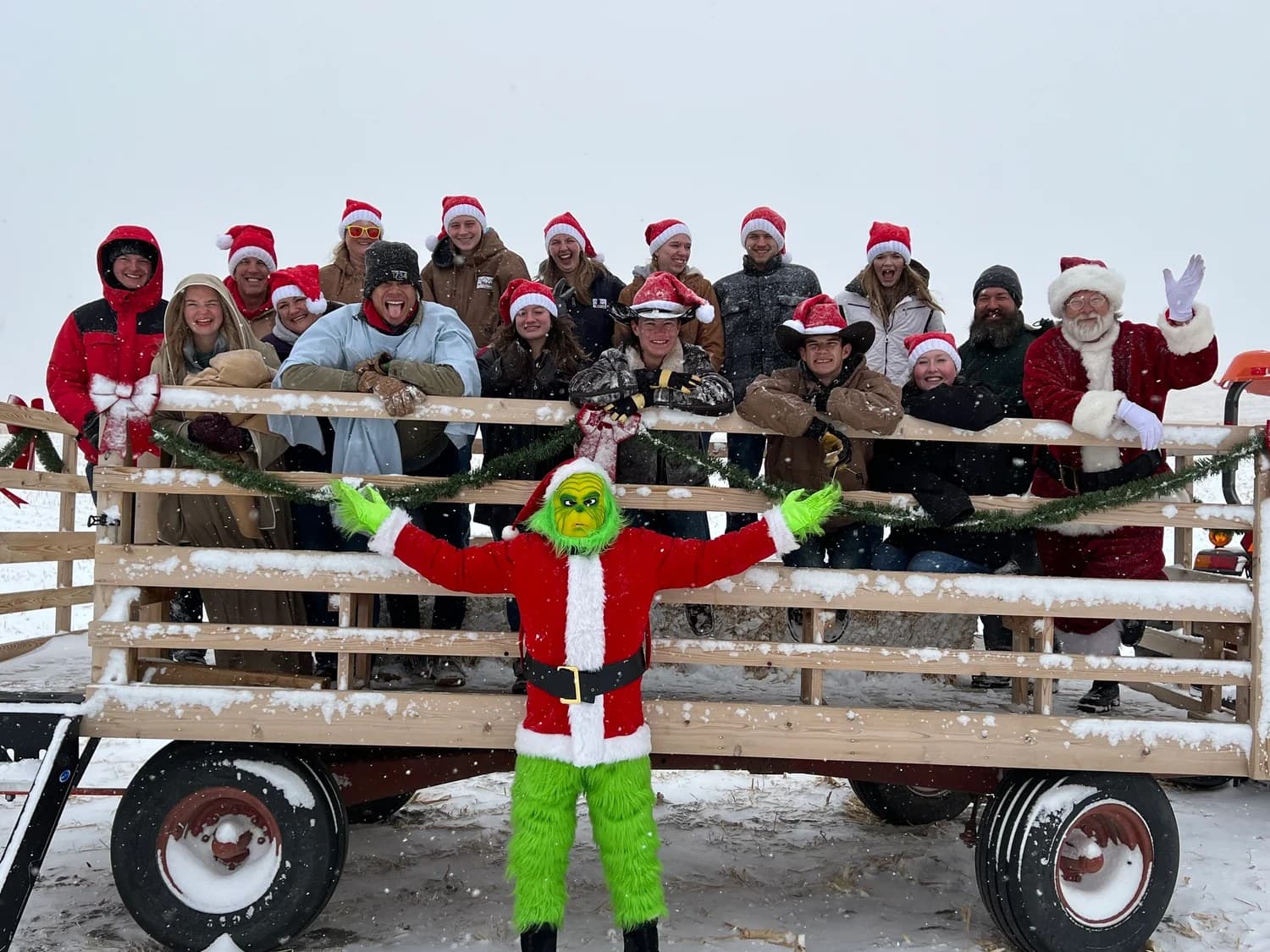 The Patch crew in Santa hats on the hay wagon in the snow, with Santa and the Grinch